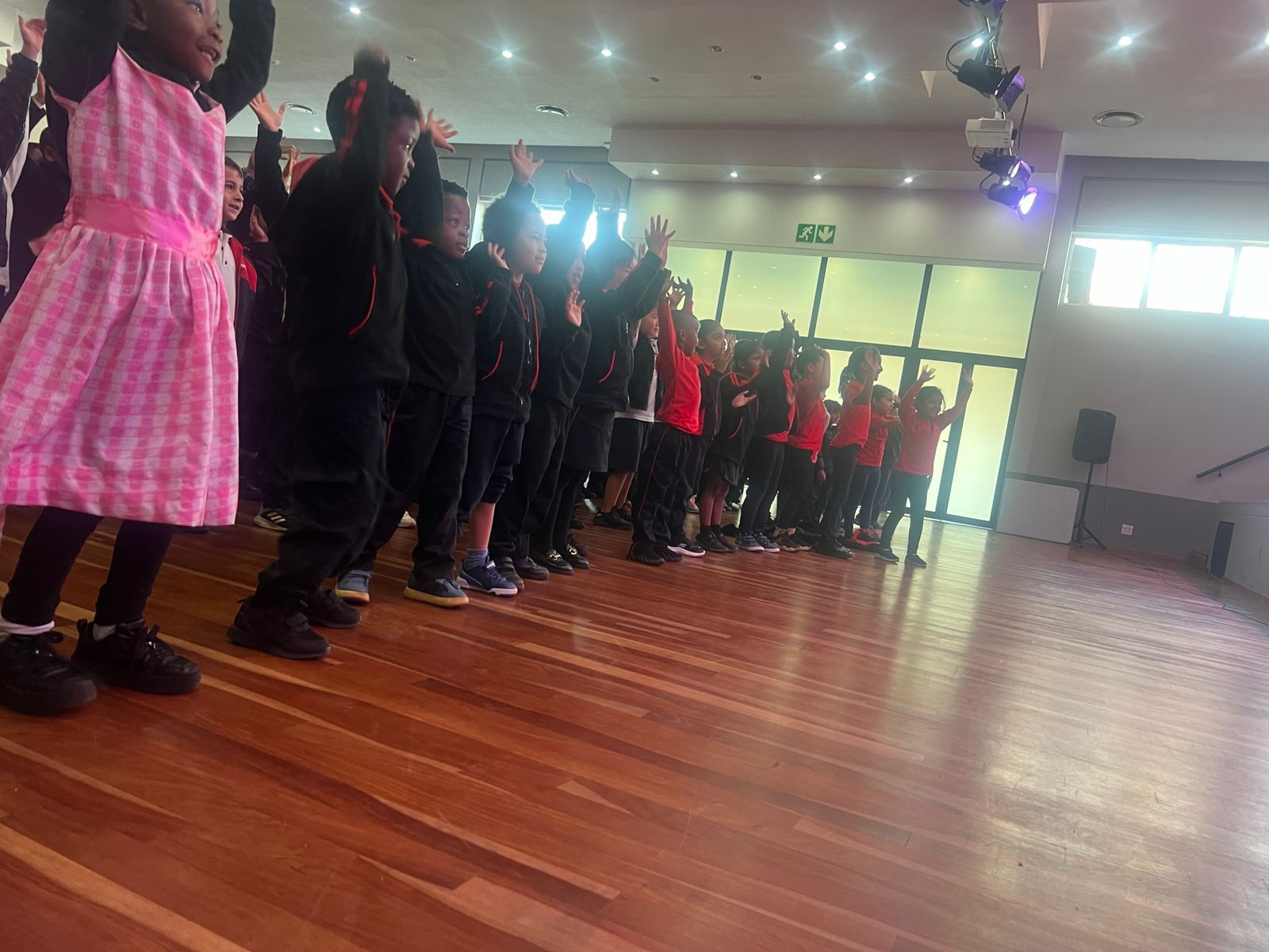 A group of children are standing on a wooden floor in a room.