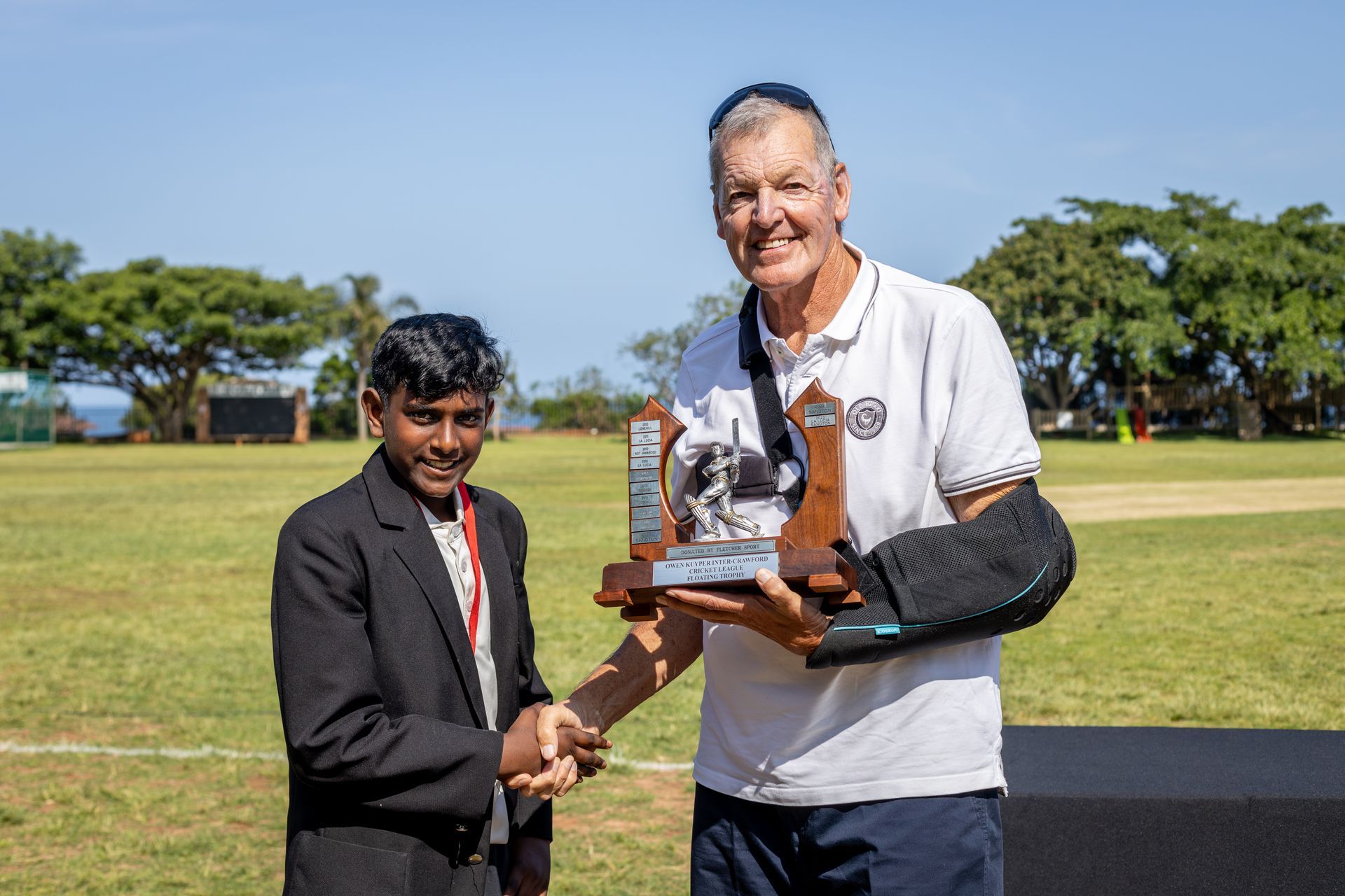 A man is shaking hands with a boy while holding a trophy.