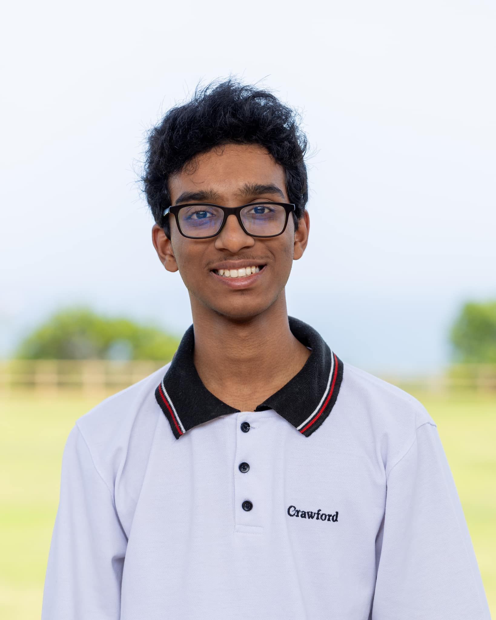 A young man wearing glasses and a white polo shirt is smiling for the camera.