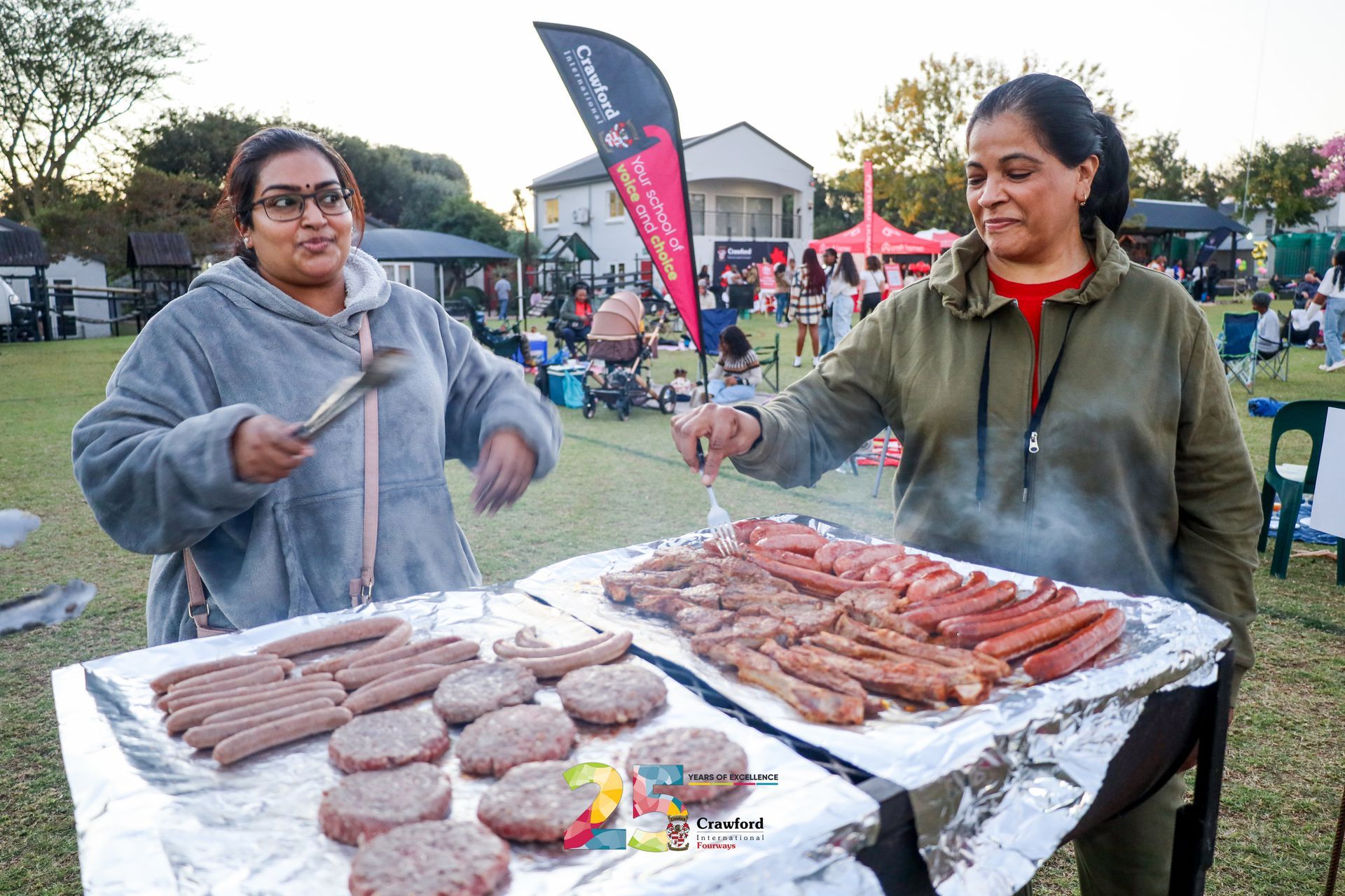 Two women are cooking food on a grill in a park.