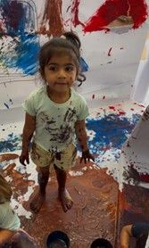 Child covered in paint stands on painted surface.