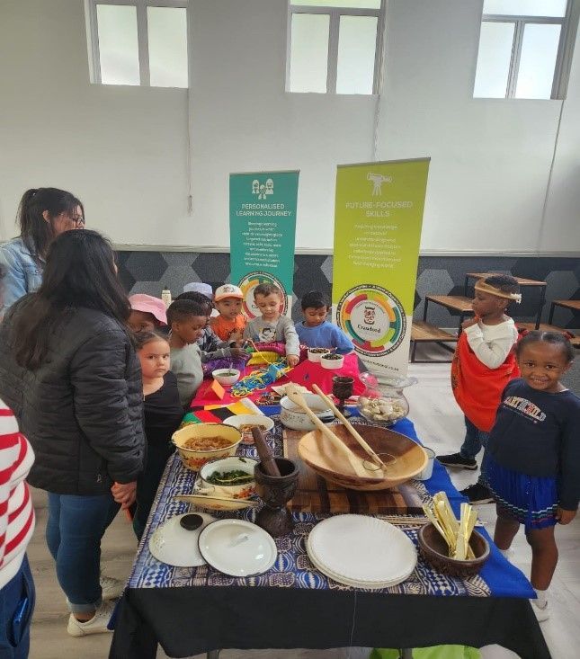 Children looking at a table of food and cultural items, with two banners in the background.