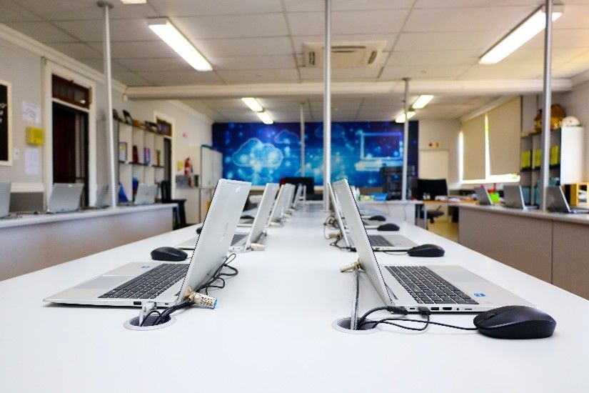 a row of laptops are sitting on a white desk in a room .