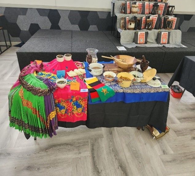 Display table with diverse textiles, pottery, and food items in a bright, colorful setting.