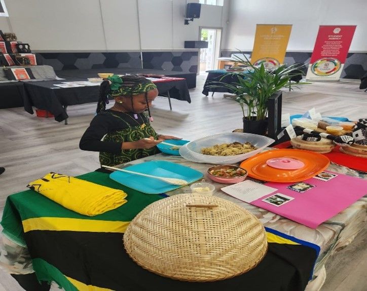 A child arranging food on a table decorated with a Tanzania flag, colorful plates, and plants inside a building.