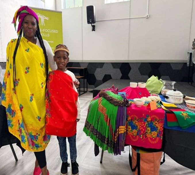 Woman and child in colorful traditional attire stand by a display of cultural items.