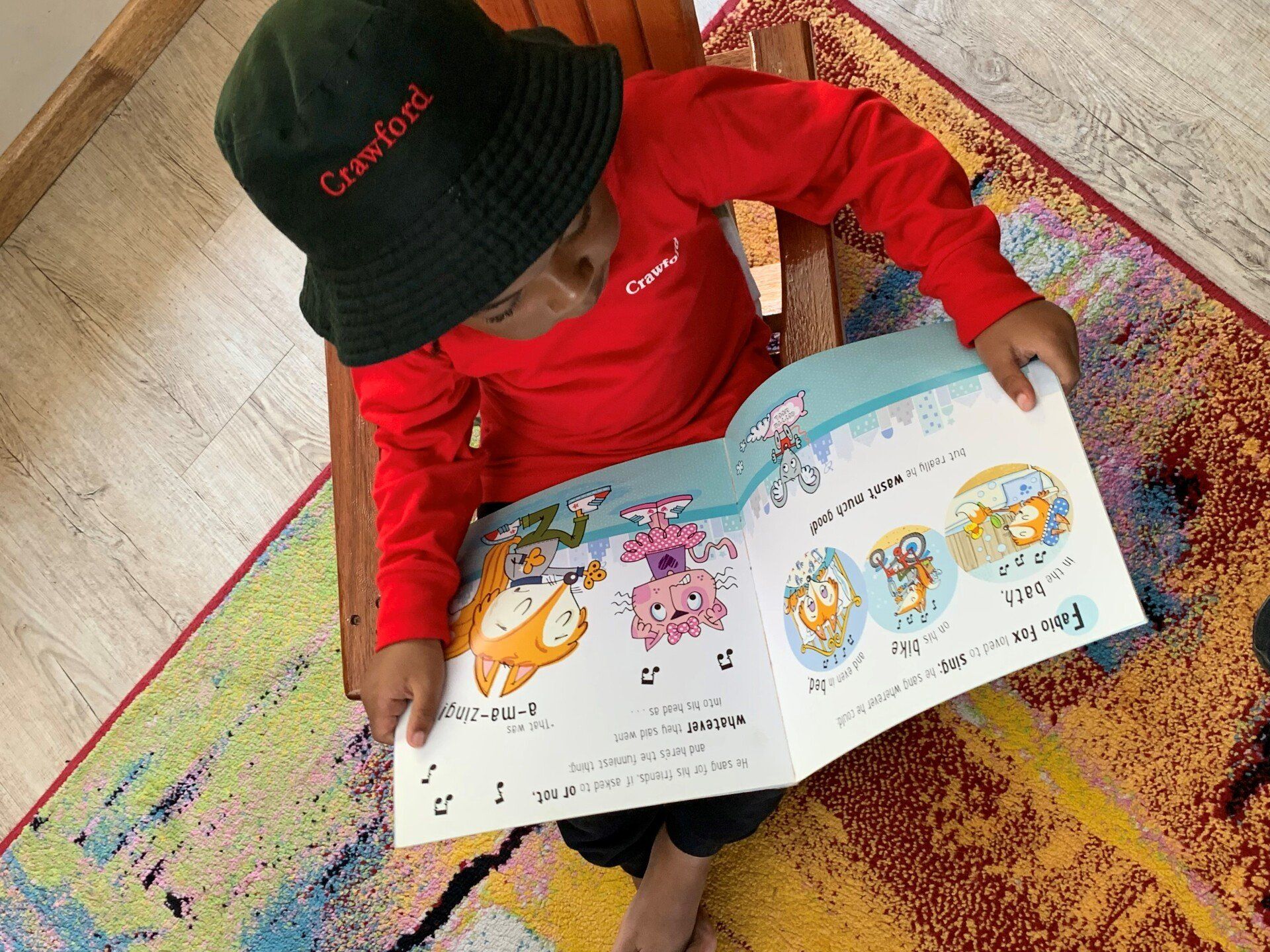 a young boy wearing a hat is reading a book .