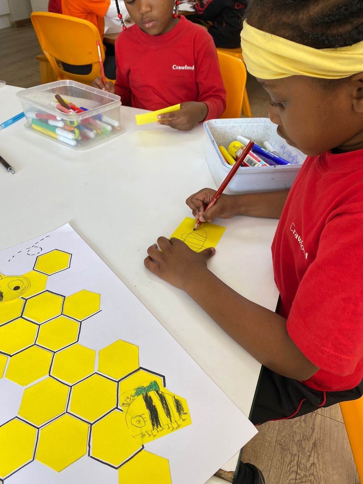 A boy in a red shirt is drawing a bee on a piece of paper