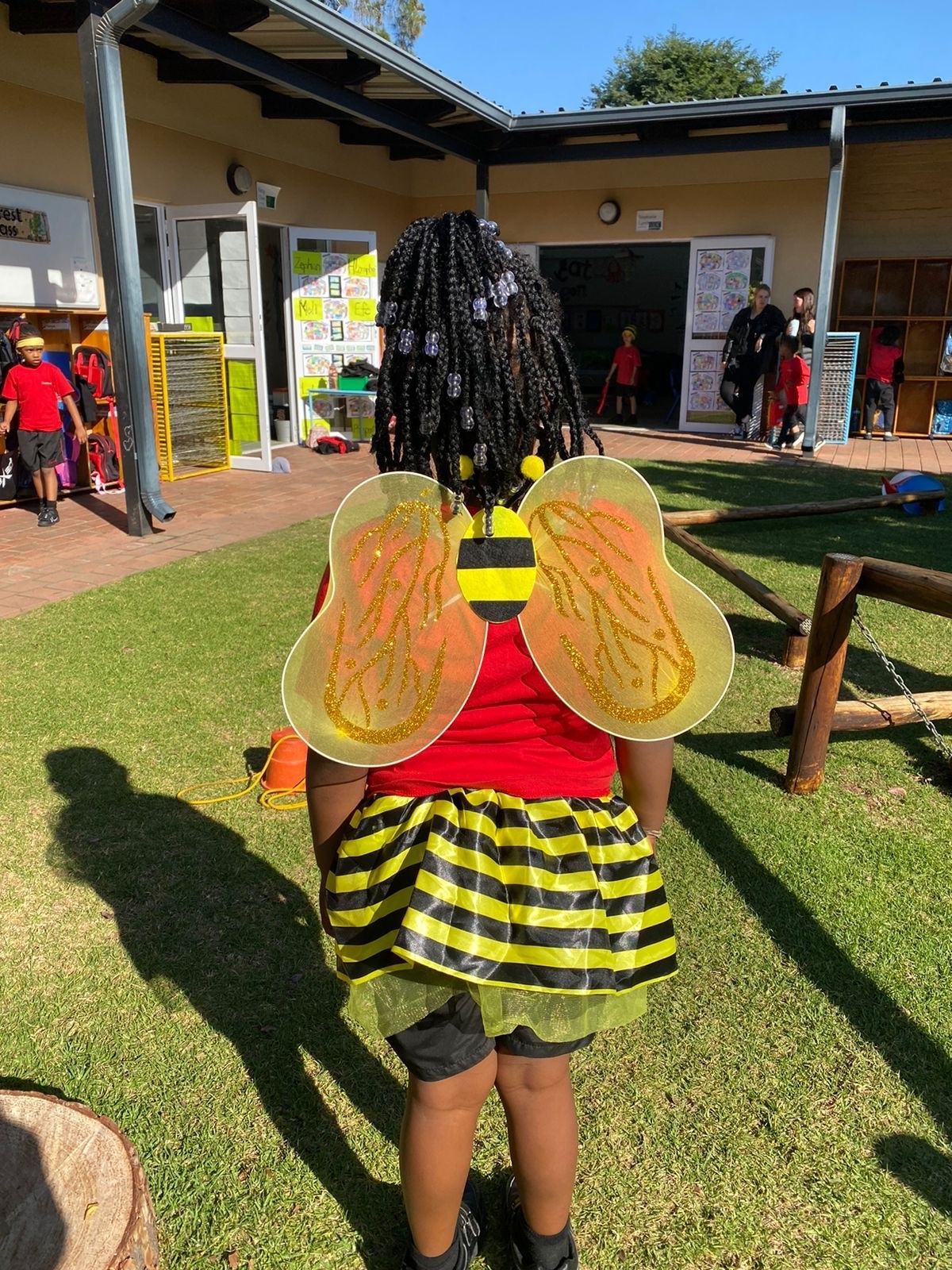 A little girl in a bee costume is standing in the grass.
