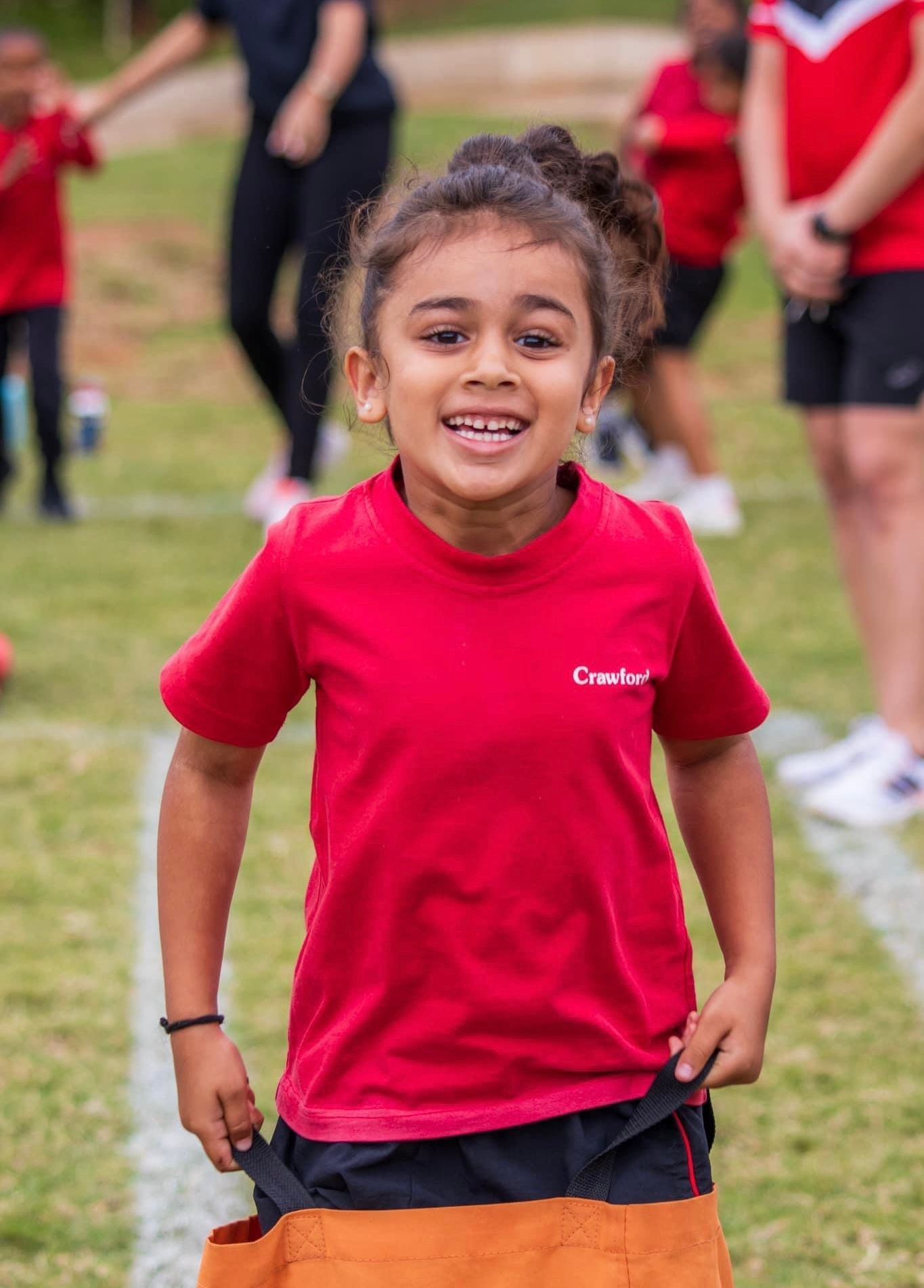 A young girl in a red shirt is smiling while standing on a field.