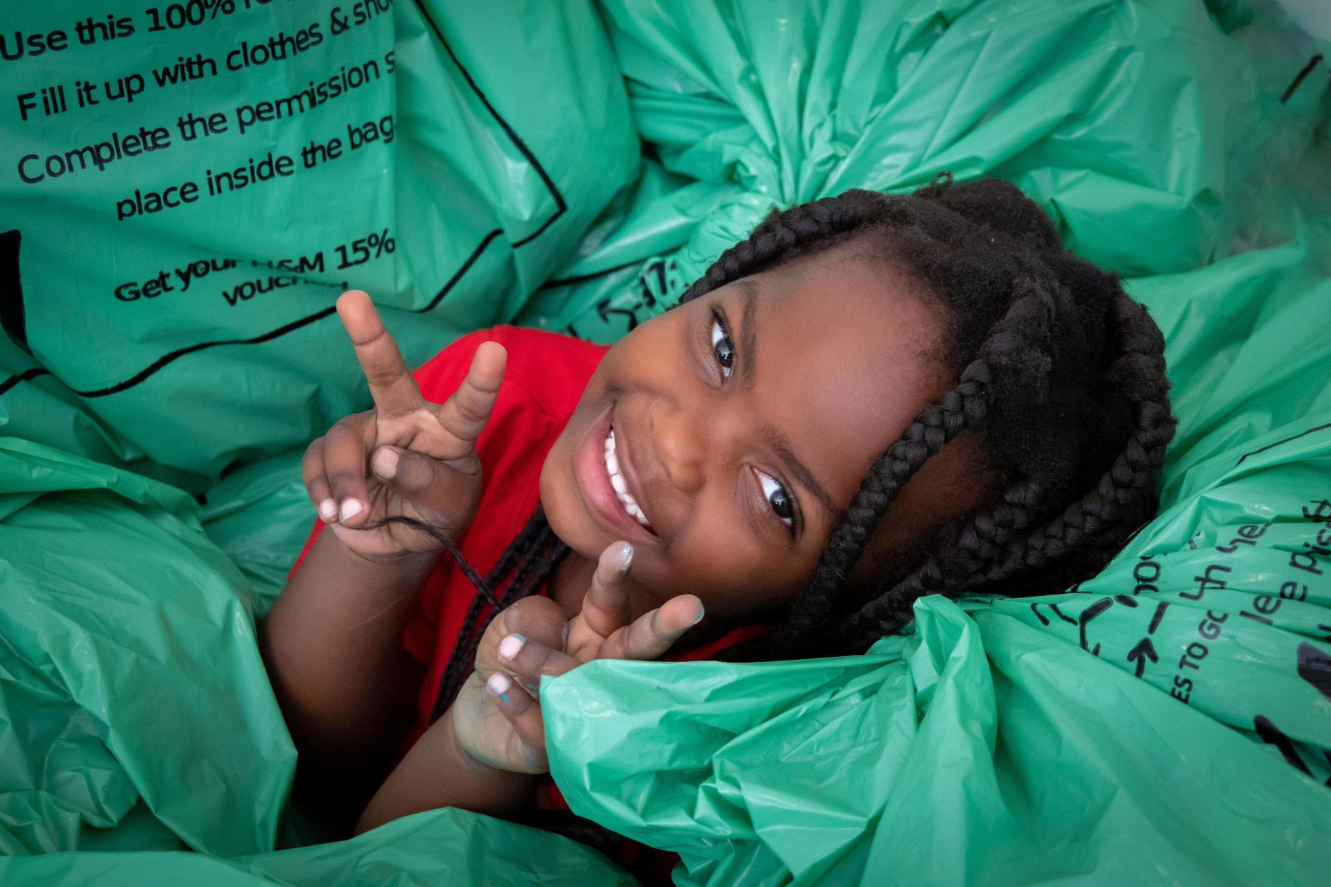 A little girl is laying in a pile of green garbage bags.