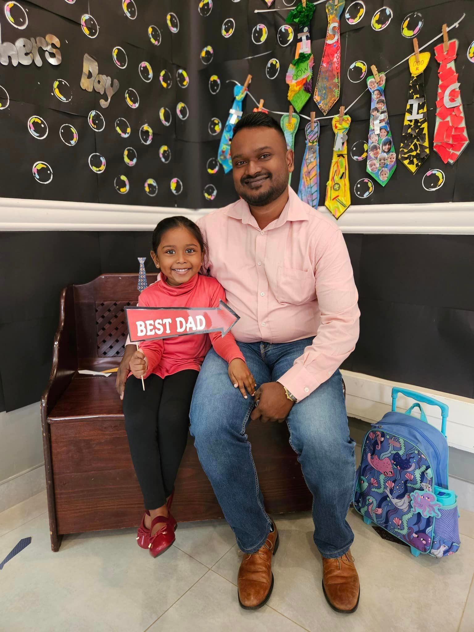 A man and a little girl are sitting on a bench holding a sign that says `` best dad ''.