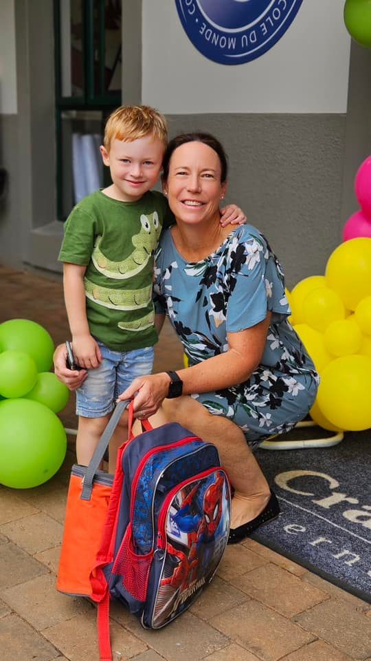 Woman and child pose together outdoors with backpack and balloons.