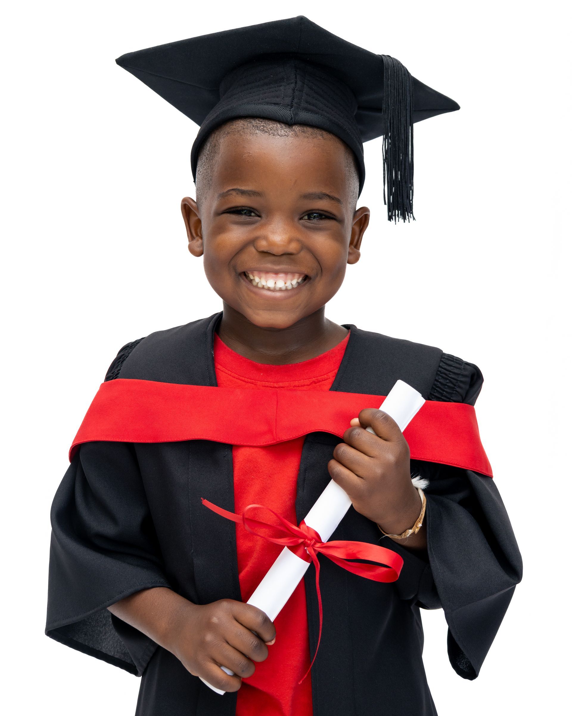 A young boy wearing a graduation cap and gown is holding a diploma.