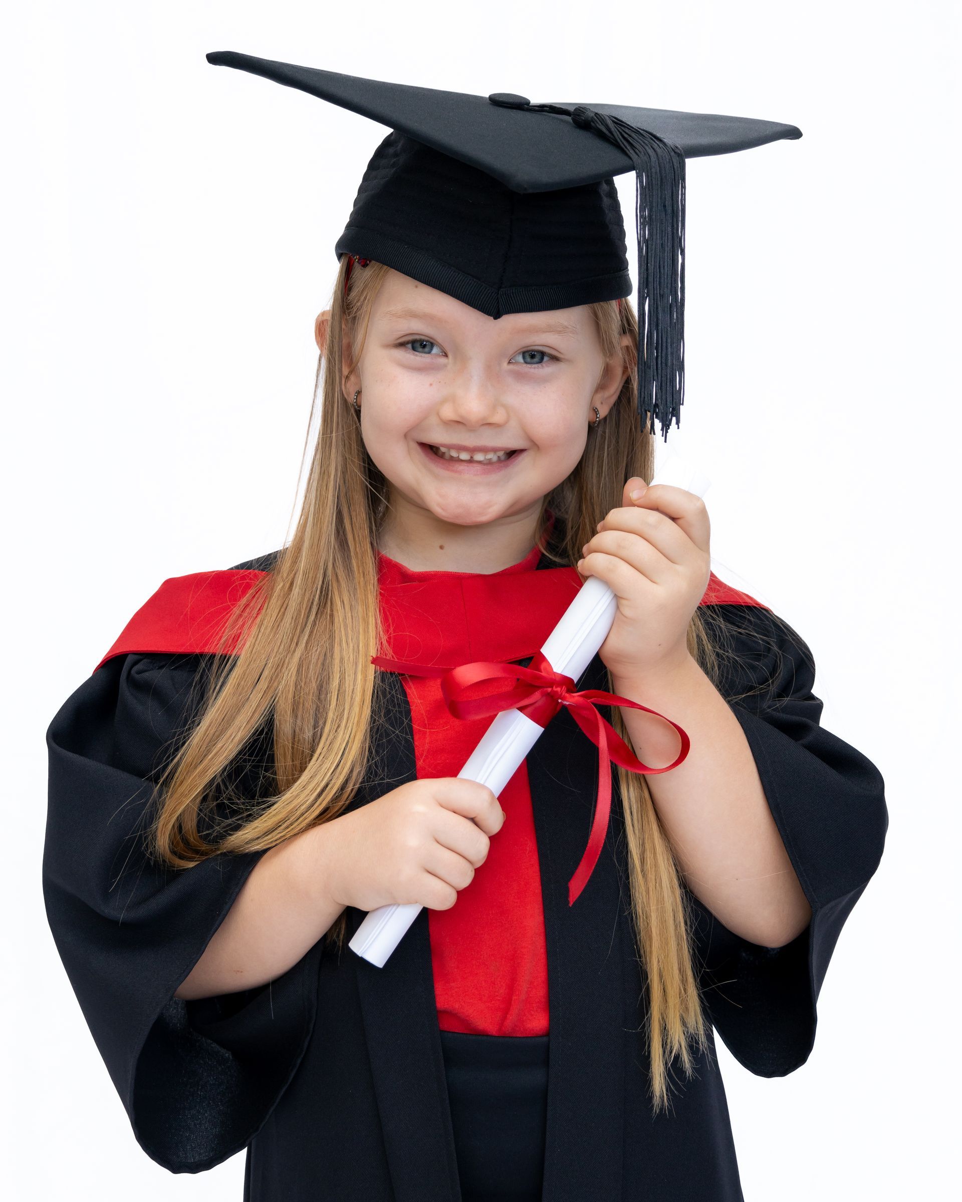 A little girl in a graduation cap and gown is holding a diploma.
