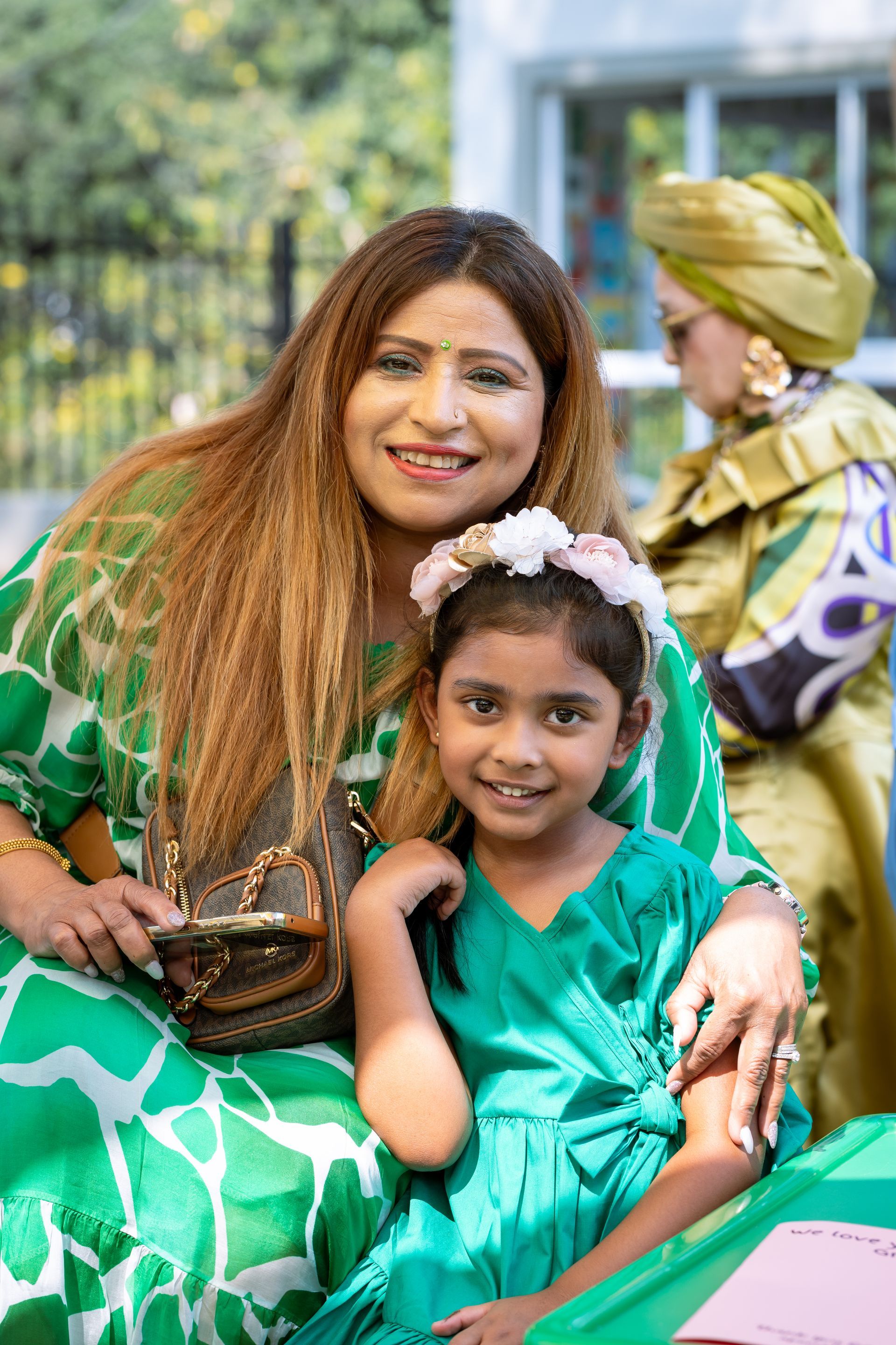 A woman in a green dress is sitting next to a little girl in a green dress.