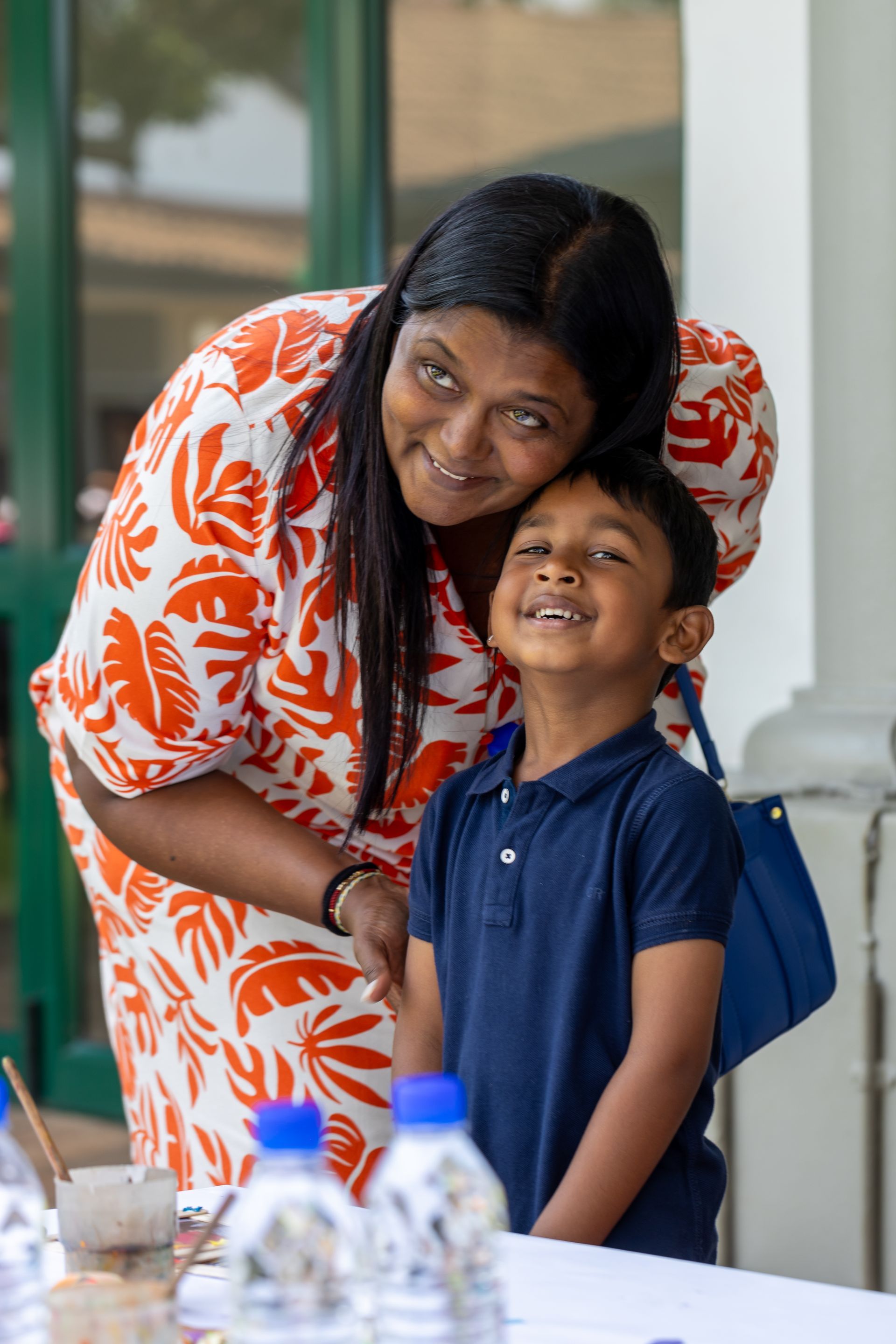 A woman is hugging a young boy who is sitting at a table.