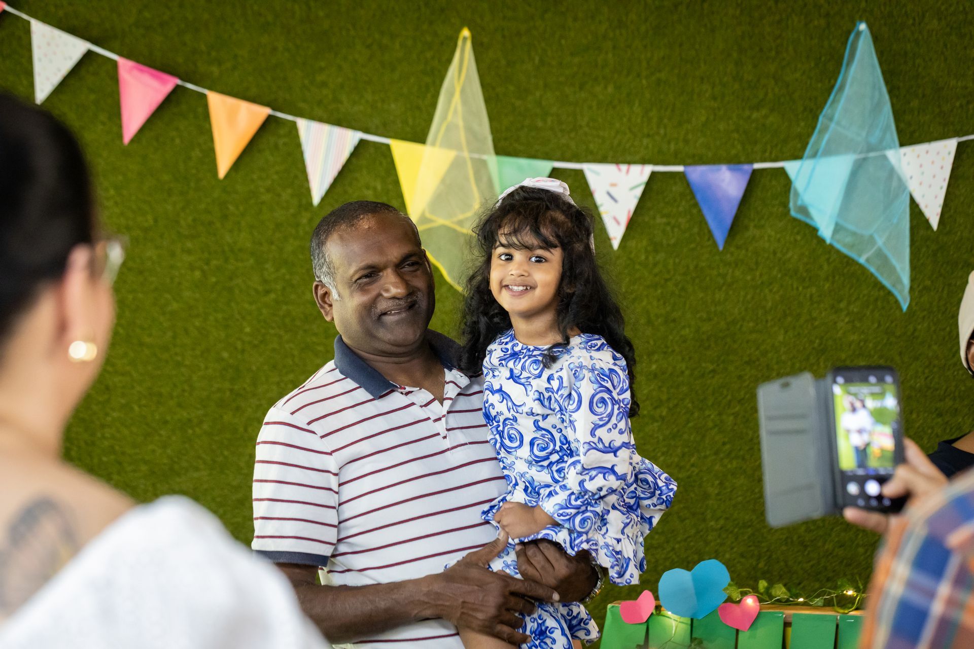 A man is holding a little girl and a woman is taking a picture of them.