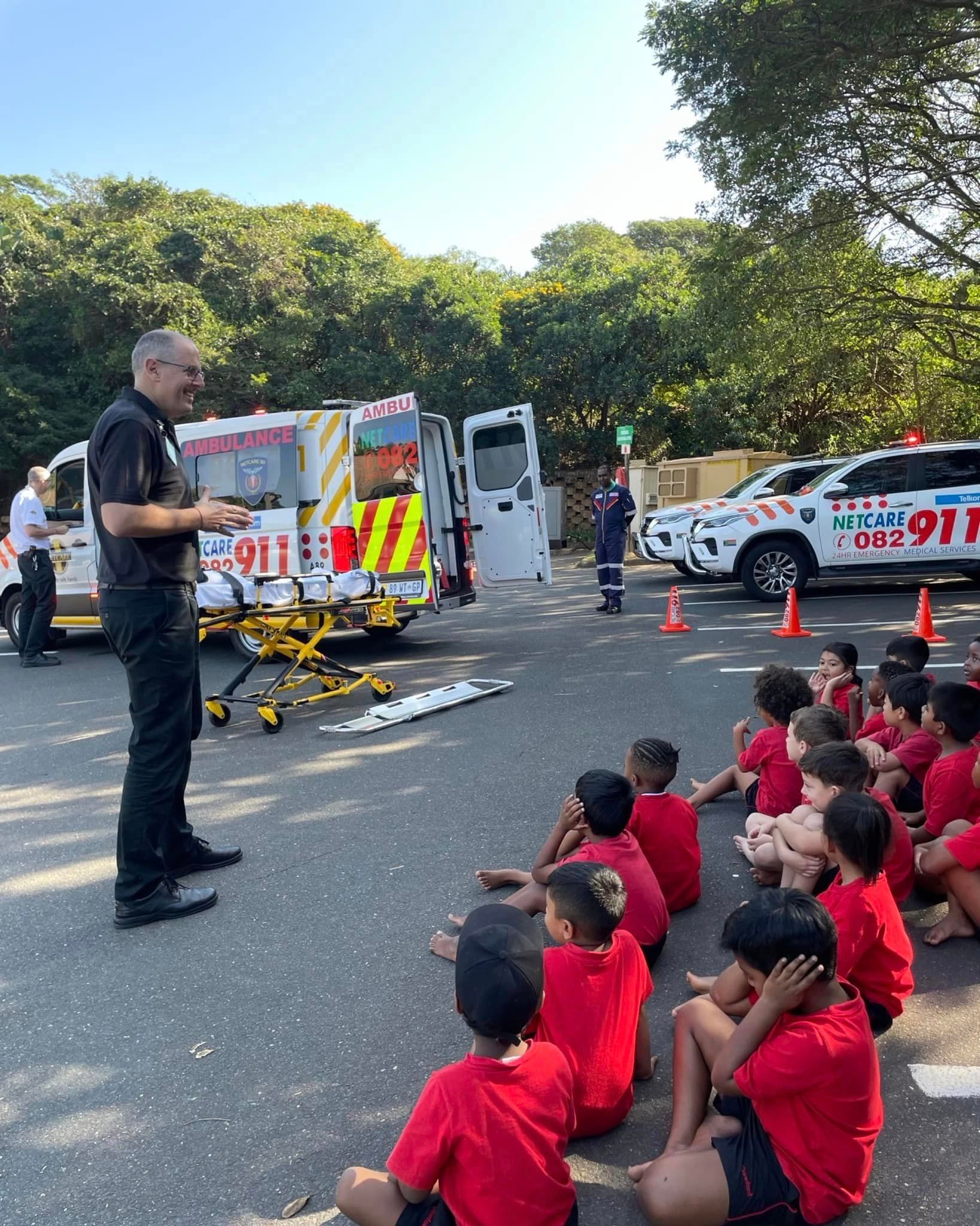A group of children are sitting on the ground in front of an ambulance.