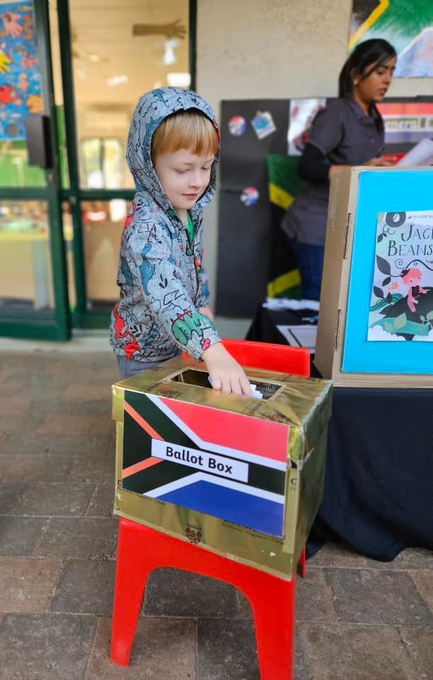 A young boy is putting a ballot in a box with the south african flag on it.