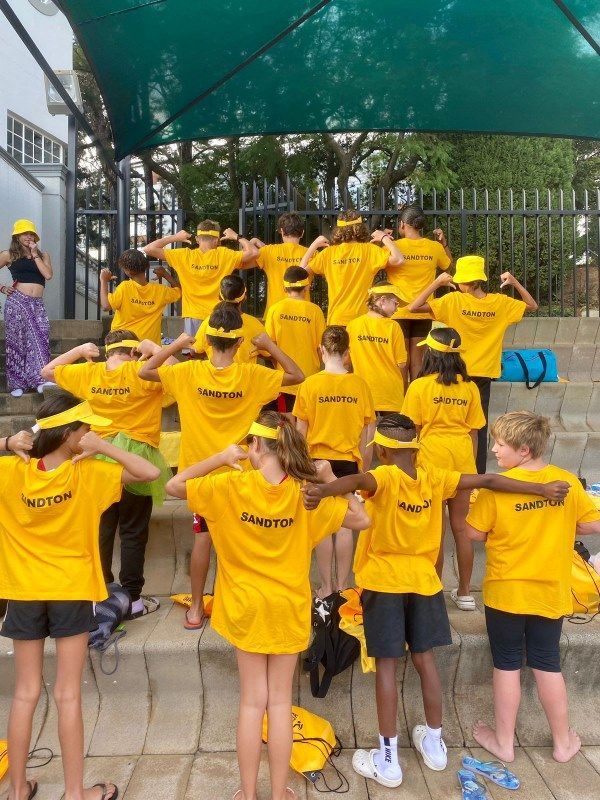 A group of children wearing yellow shirts and hats are standing under a canopy.