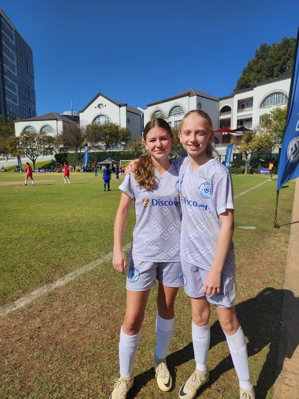 Two young girls are posing for a picture on a soccer field.