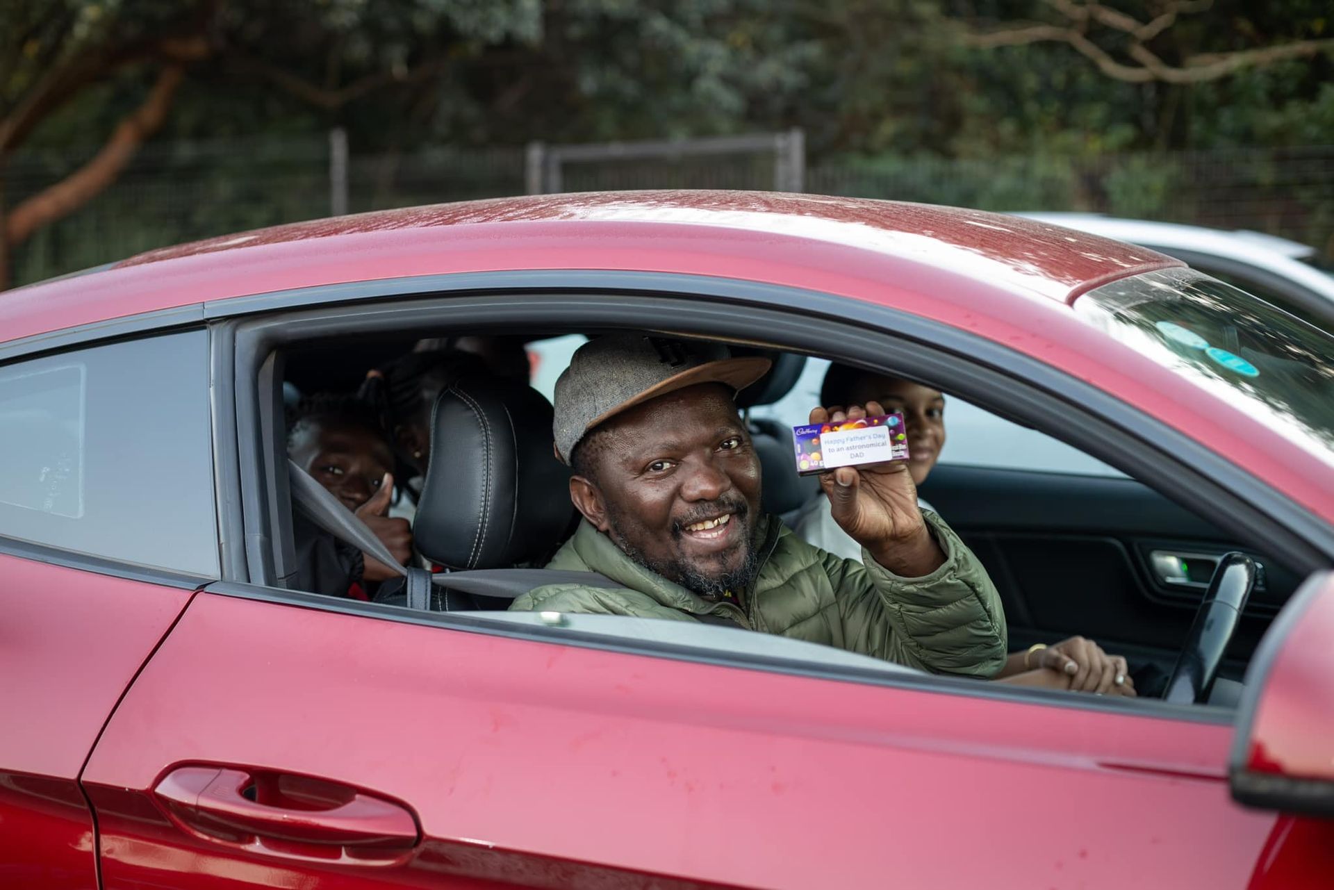 A man is sitting in a red car holding a driving license.