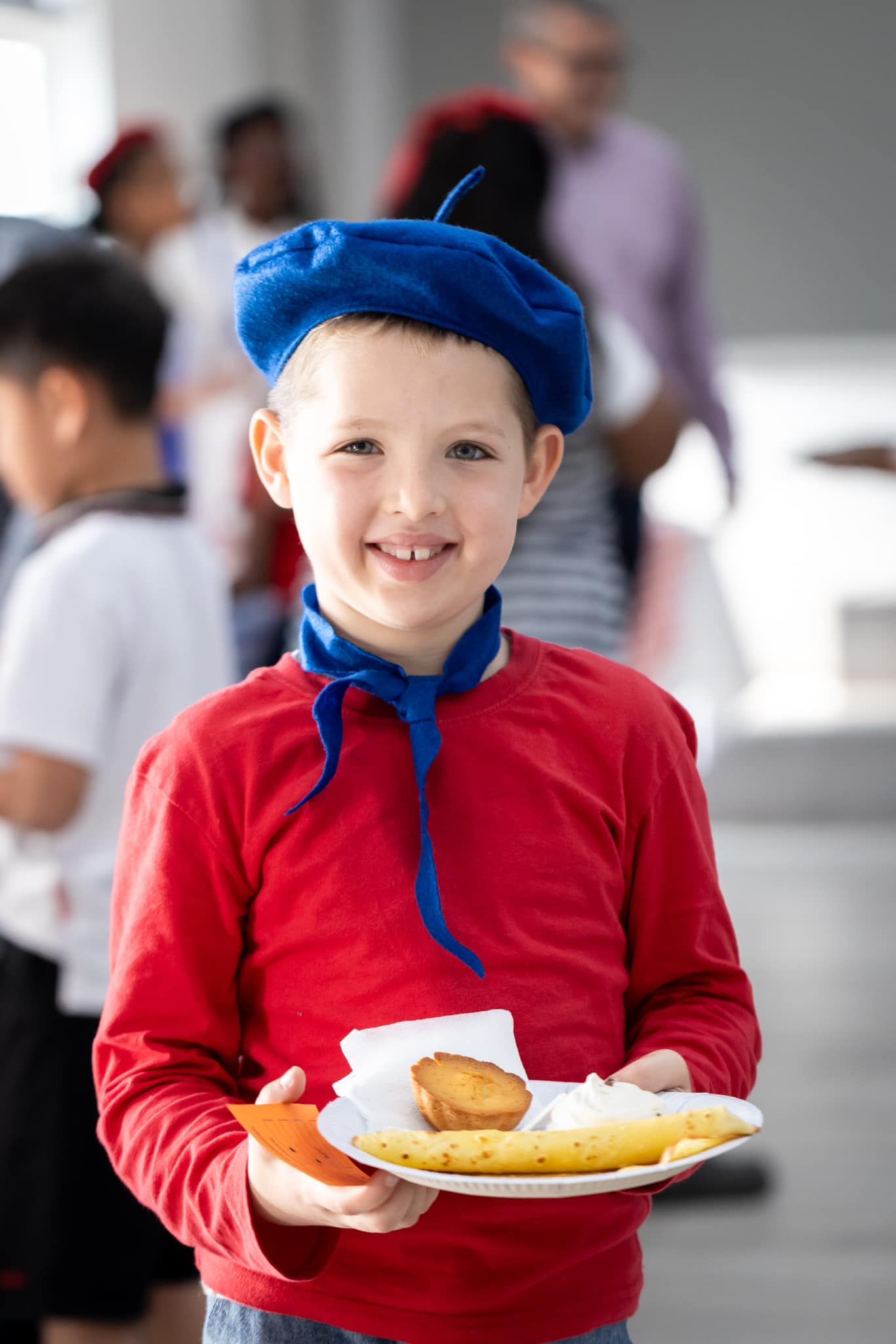 A young boy wearing a blue beret is holding a plate of food.