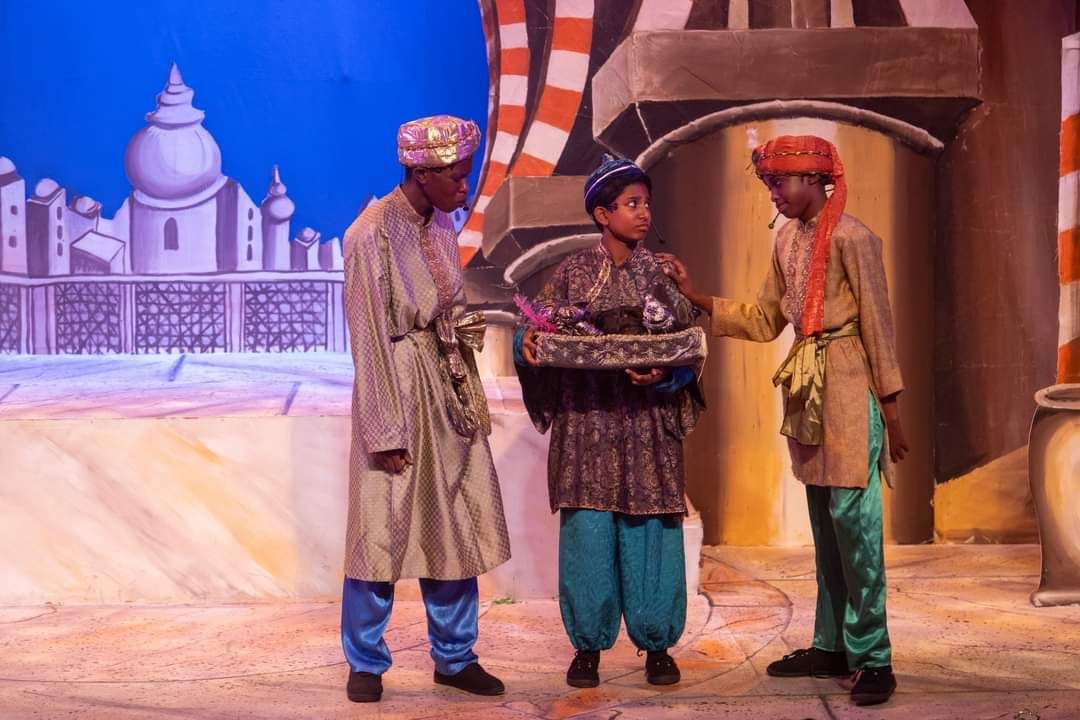 Three men are standing on a stage and one of them is holding a box.