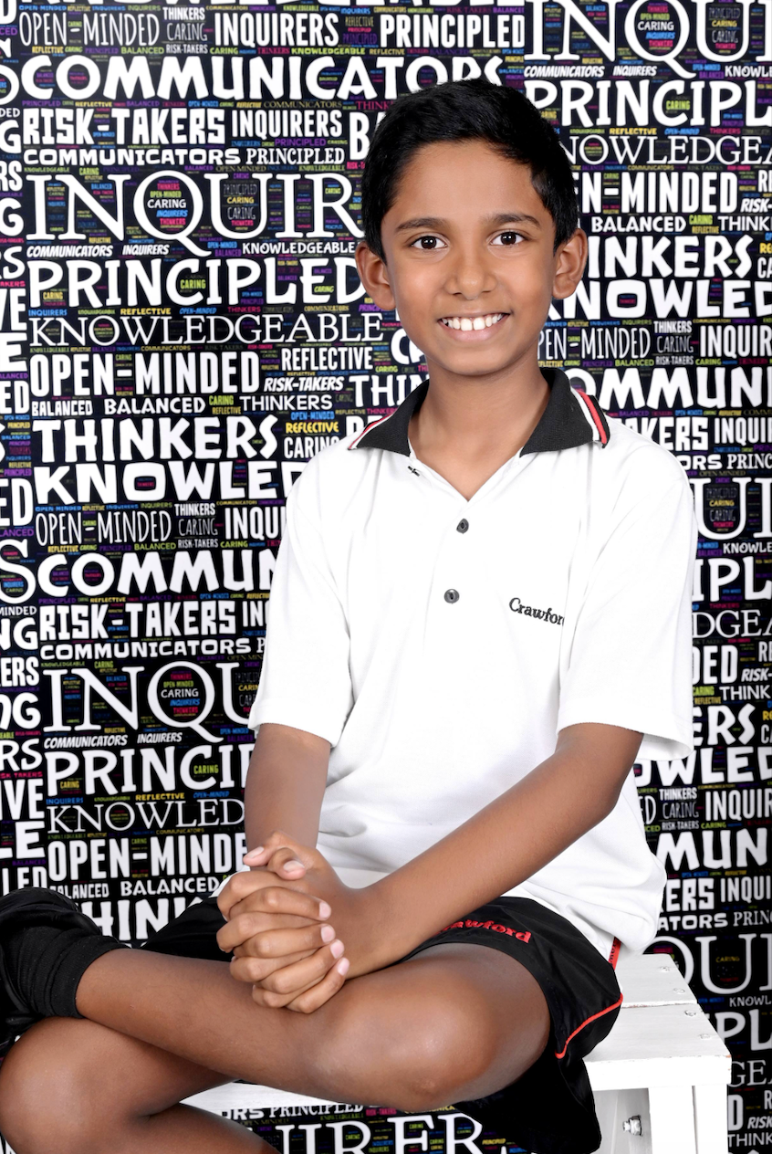 A young boy is sitting in front of a wall with words on it.