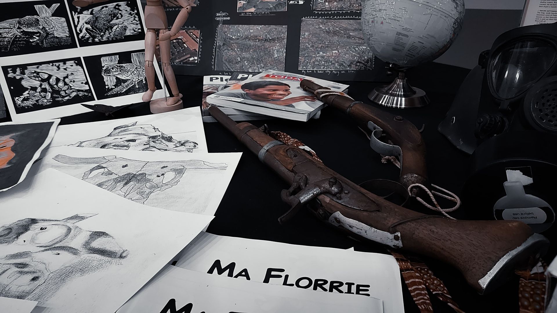 Still life: antique firearms, sketches, magazines, gas mask, and a globe on a black surface.