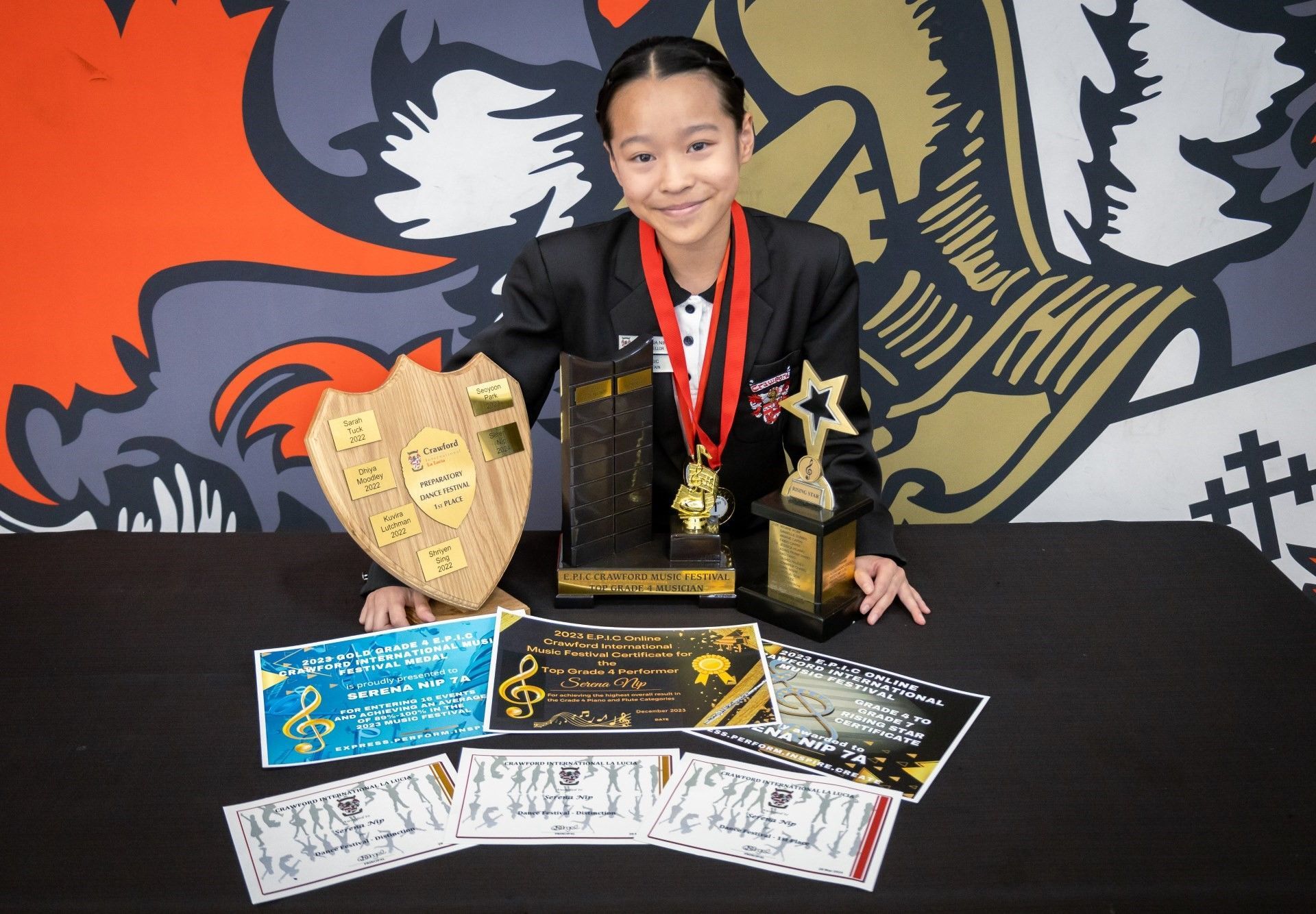 A young girl is sitting at a table with trophies and medals.