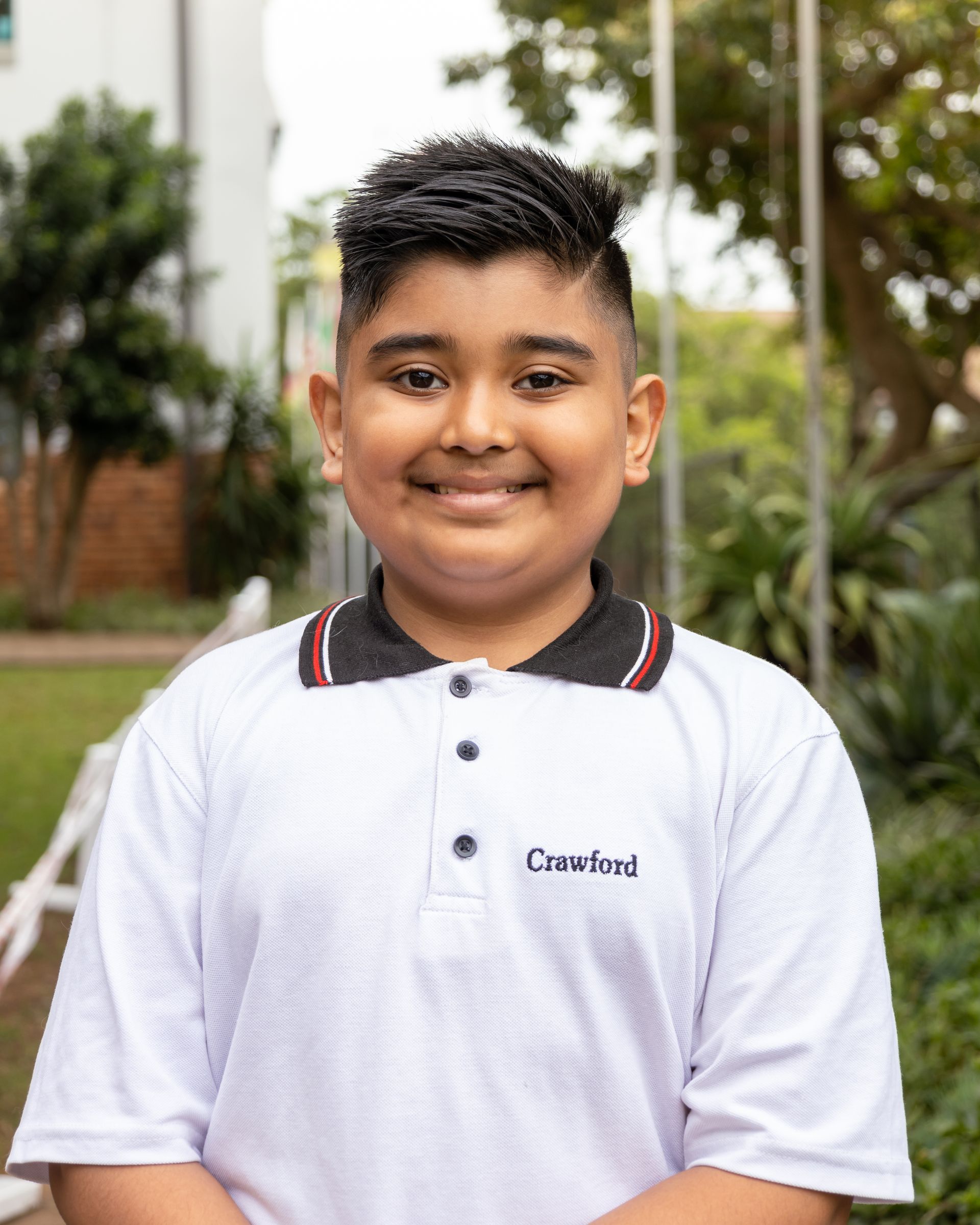 A young boy wearing a white polo shirt is smiling for the camera.