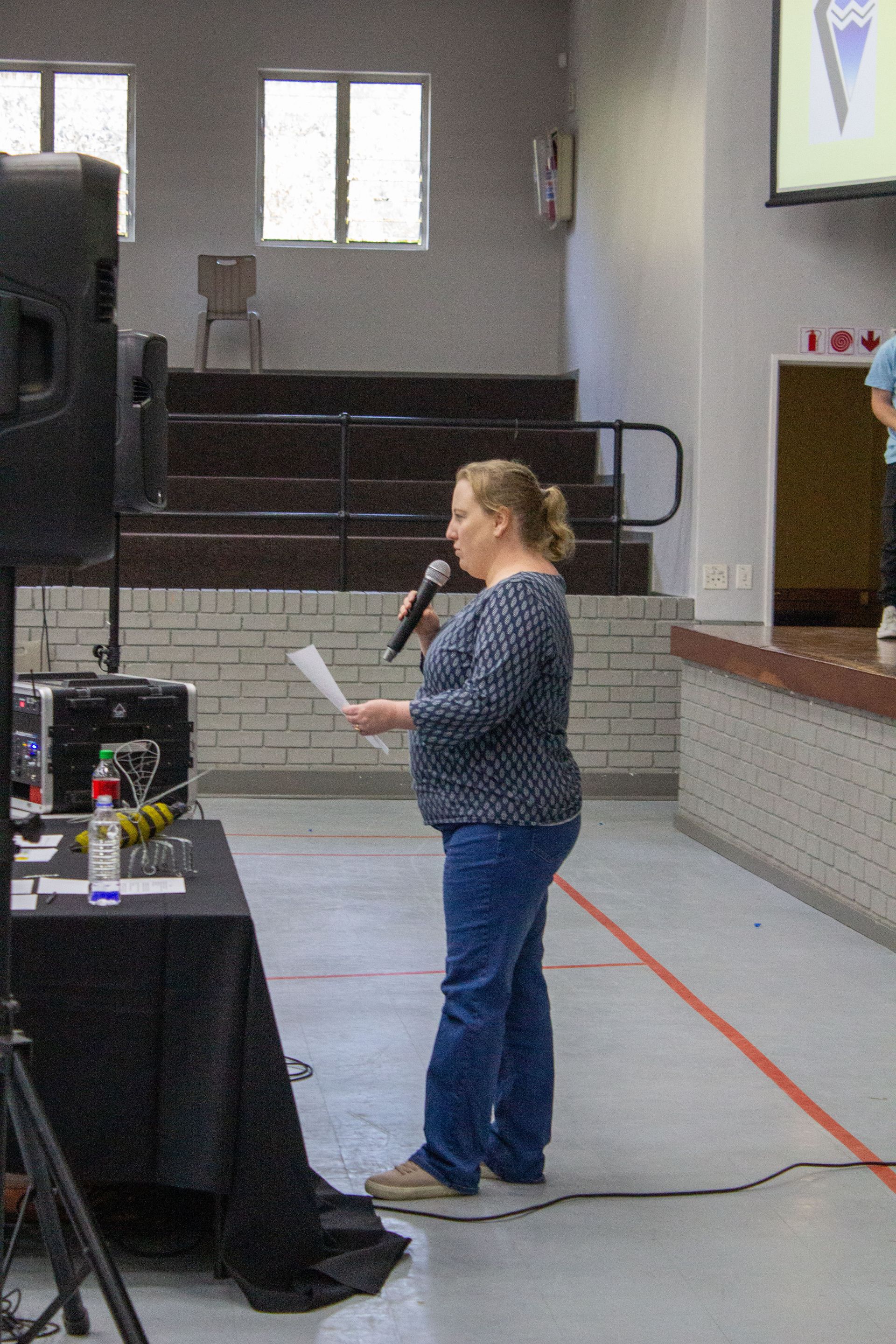 A woman is standing in front of a microphone holding a piece of paper.