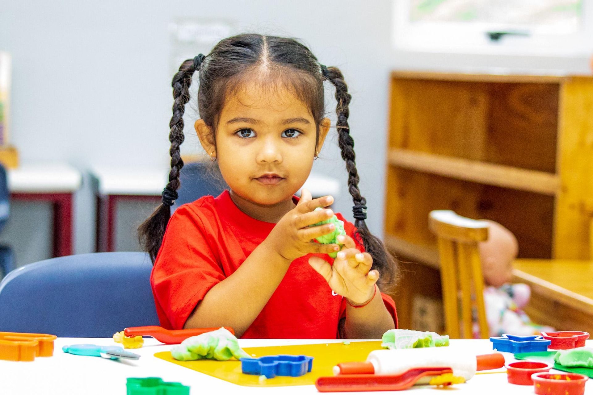 Girl with braids playing with playdough at a table in a classroom.