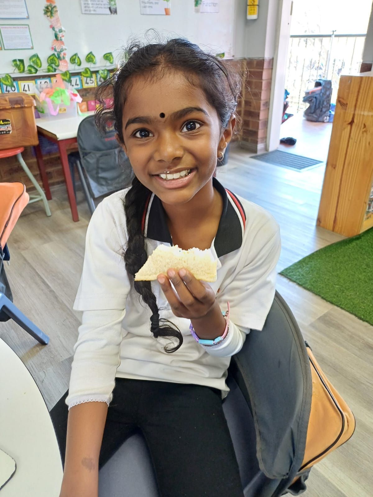 A young girl is sitting at a table eating a piece of bread.