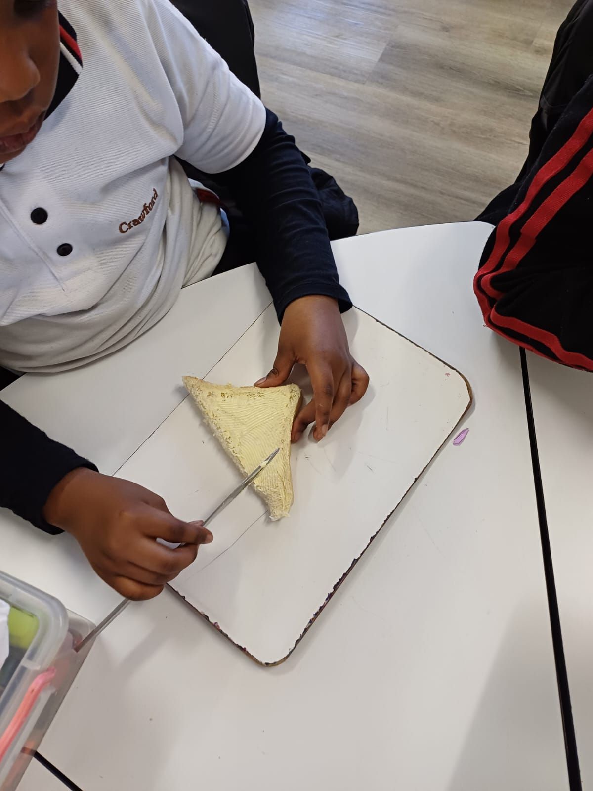 A child is cutting a piece of bread on a white board