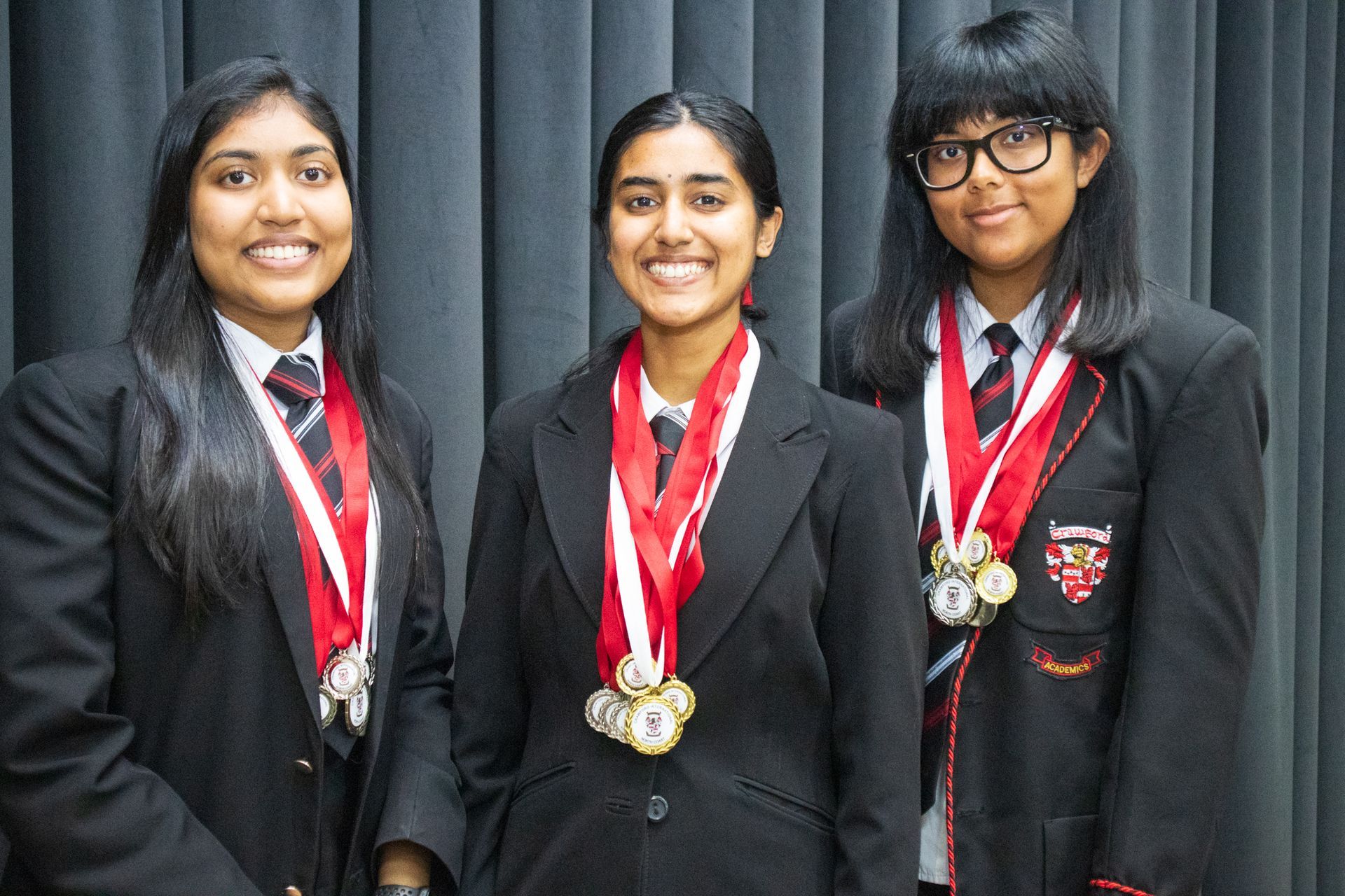Three girls in school uniforms with medals around their necks are posing for a picture.