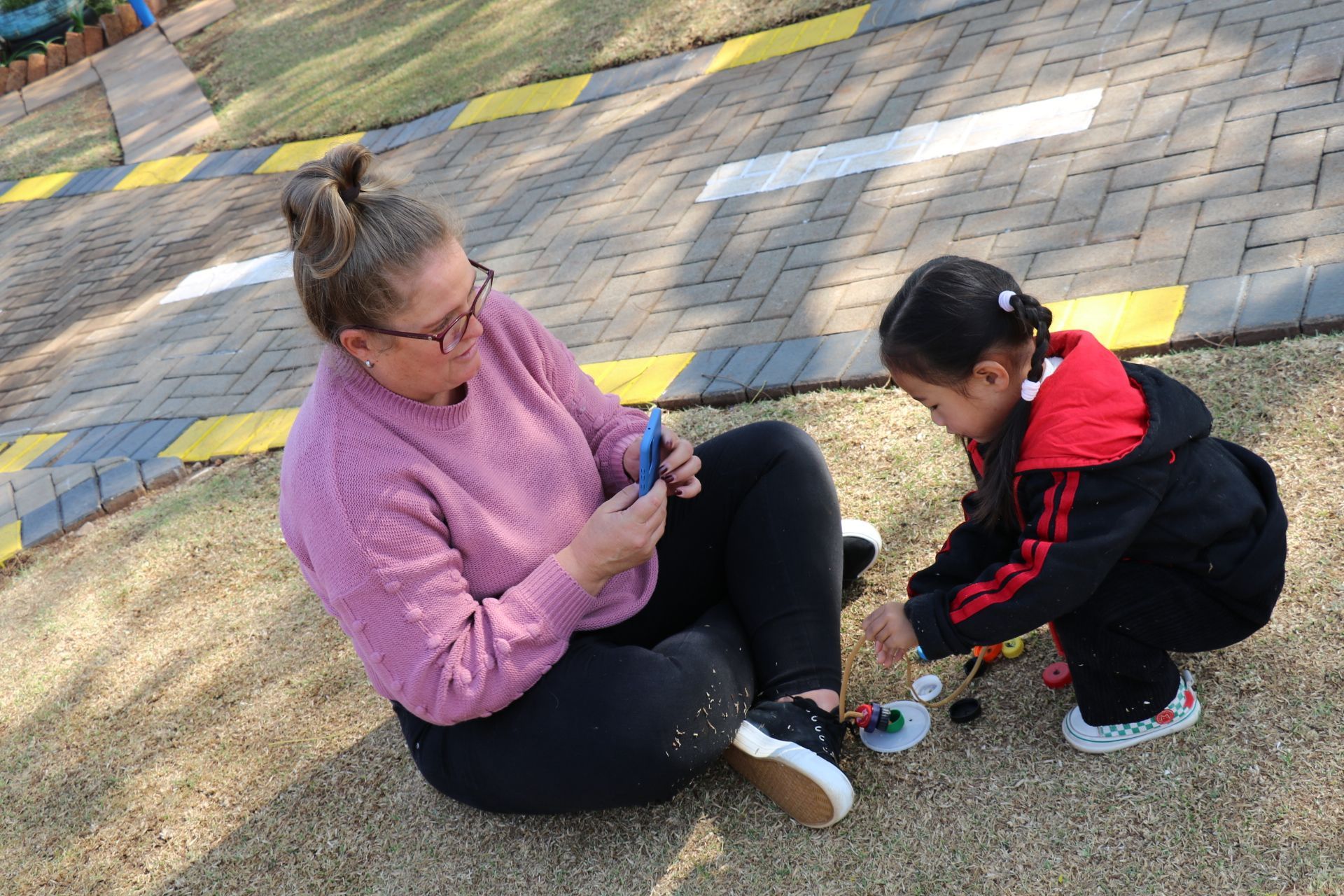 A woman and a little girl are sitting on the ground playing with toys.