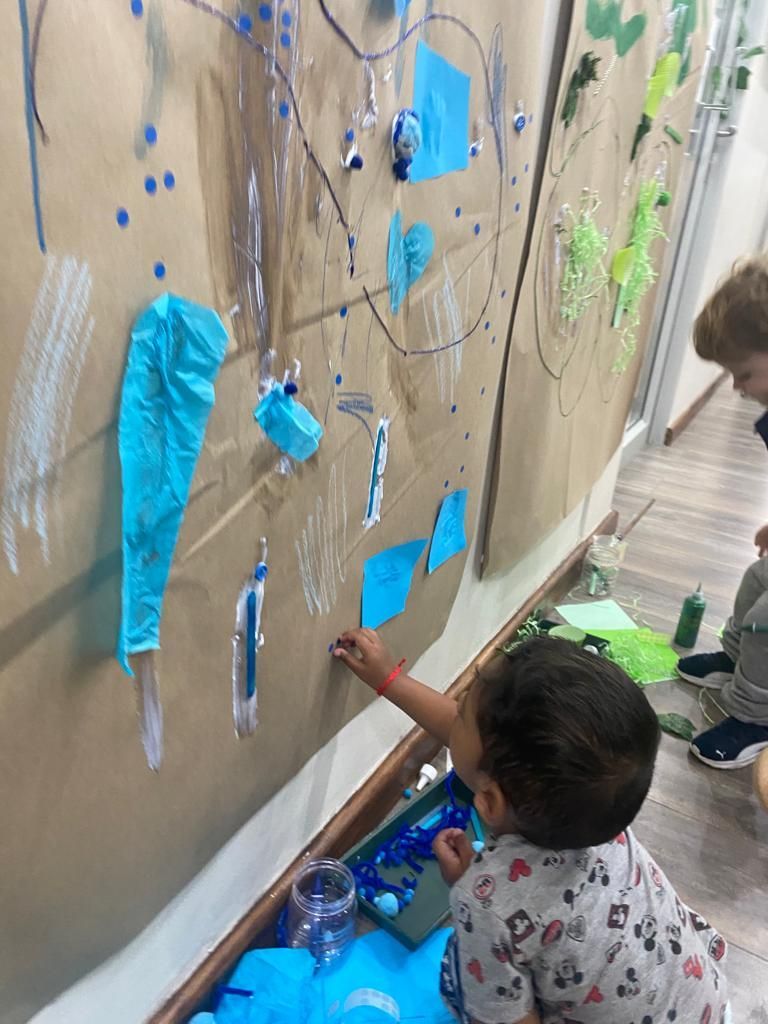 A little boy is painting on a wall with blue paint.