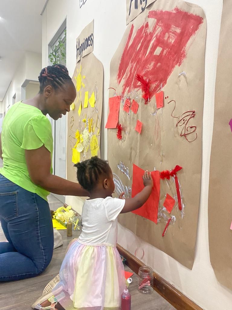 A woman is kneeling down next to a little girl who is painting on a wall.