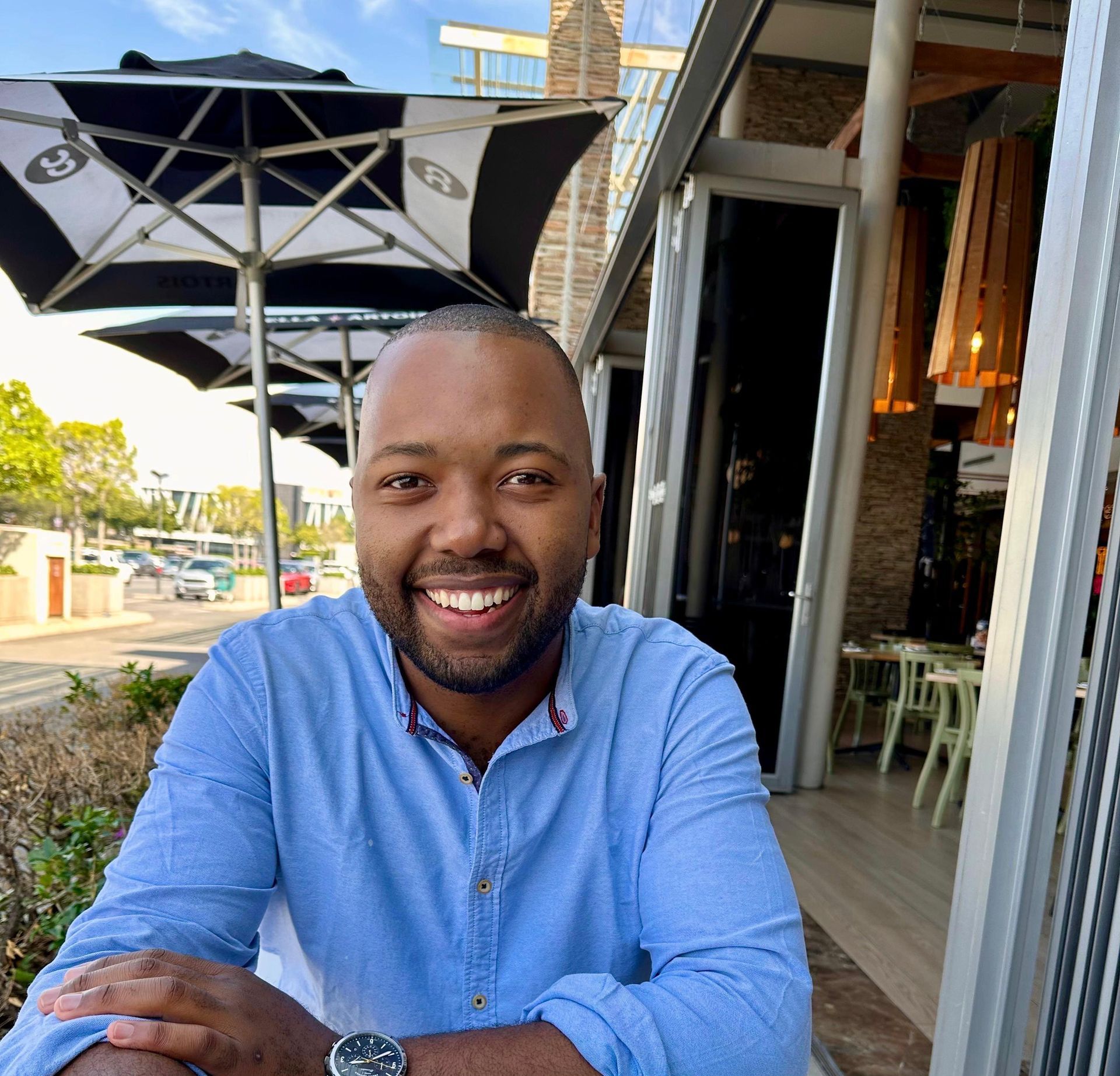A man in a blue shirt is smiling while sitting under an umbrella