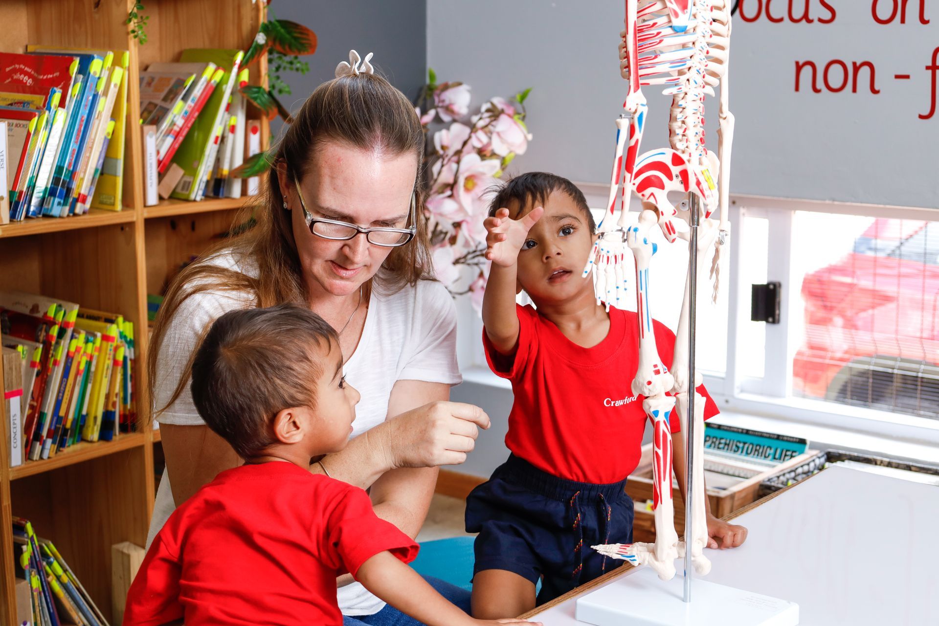 A woman and two children are looking at a model of a skeleton.