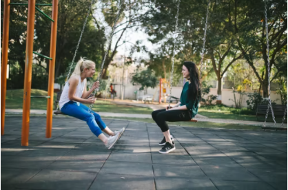 Two young women sitting opposite each other on swings, living your best life