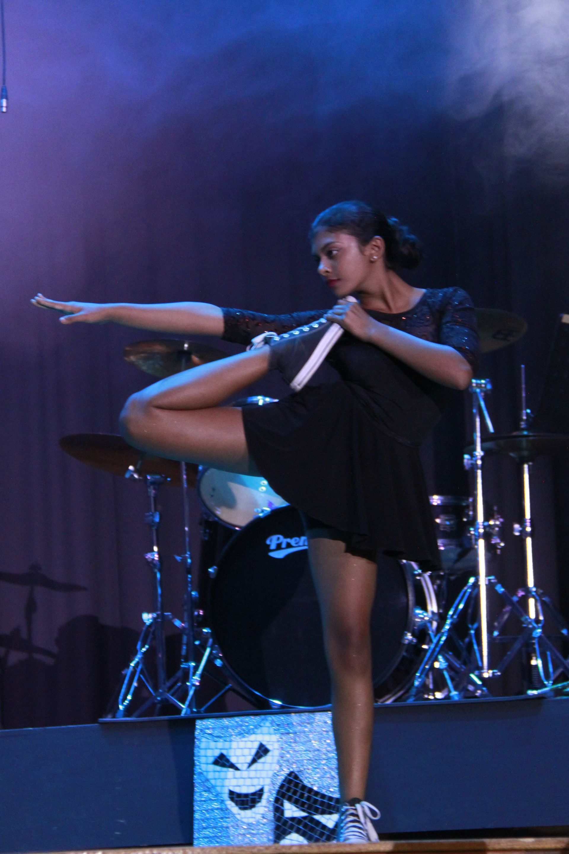 A woman is standing on one leg in front of a drum set