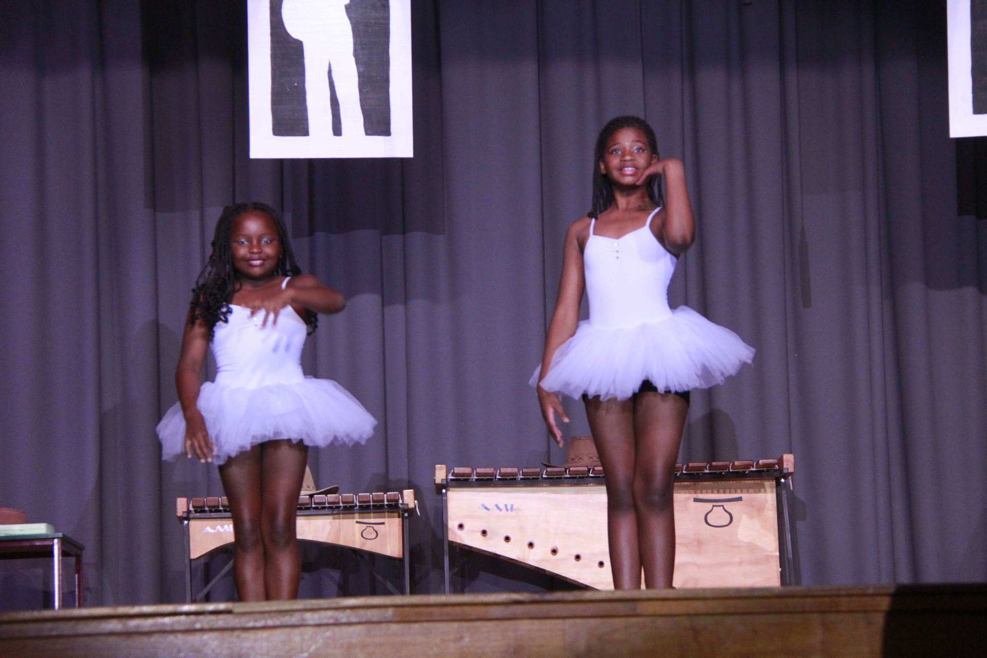 Two young girls in white tutus are dancing on a stage