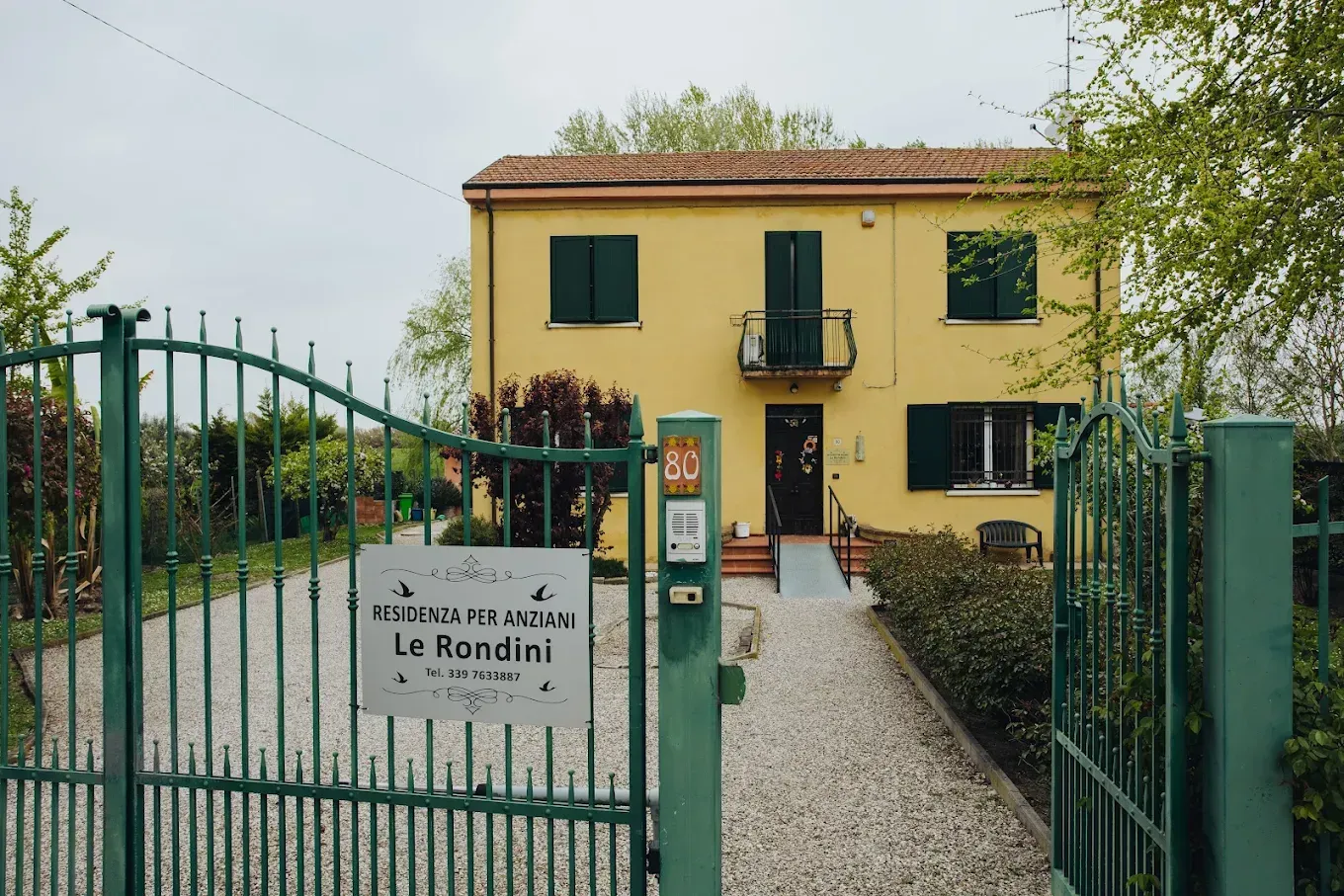 Casa gialla con cancello verde; cartello con la scritta "Le Rondini".