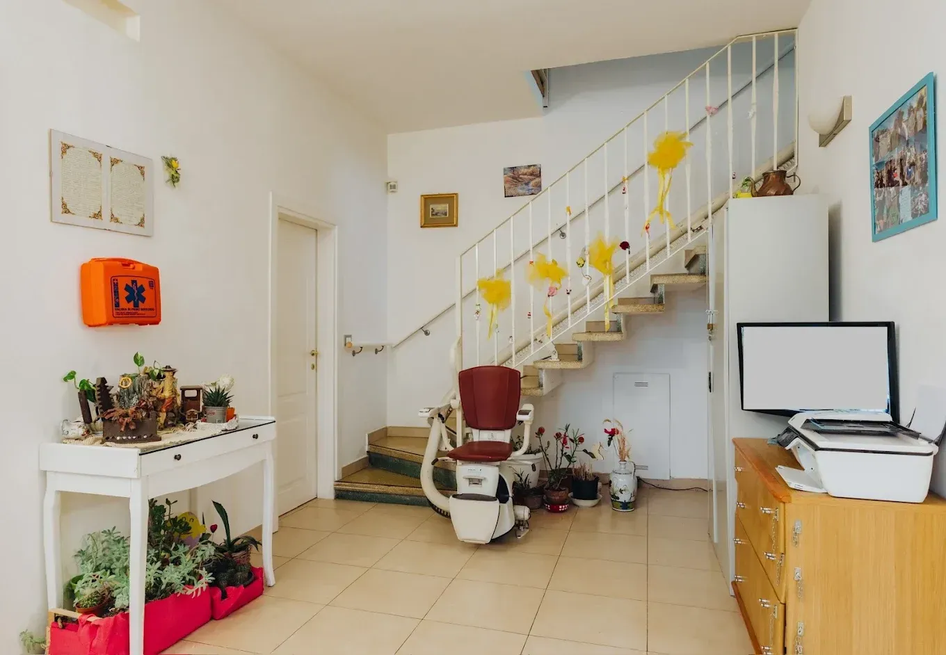 Interno con scale, un montascale e un tavolo consolle. Pareti bianche, scale in legno, una stampante.