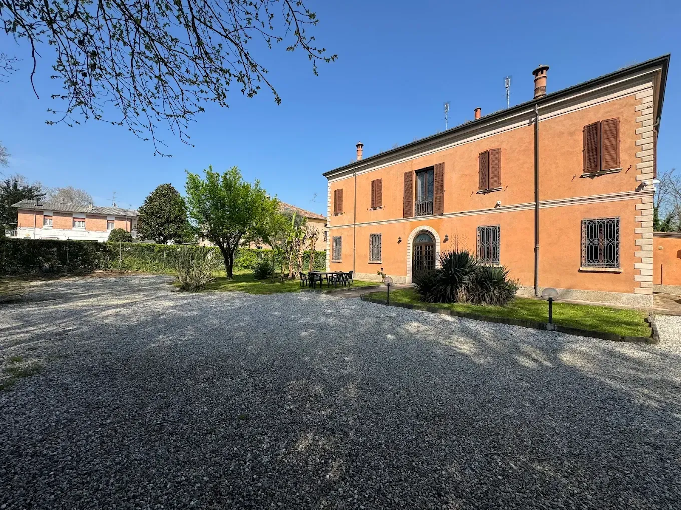 Edificio arancione a due piani con persiane marroni e un vialetto di ghiaia sotto un cielo azzurro brillante.