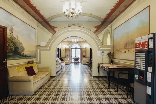 Lungo corridoio con soffitto decorato, archi, dipinti, pavimento decorato, divani e macchina per il caffè.